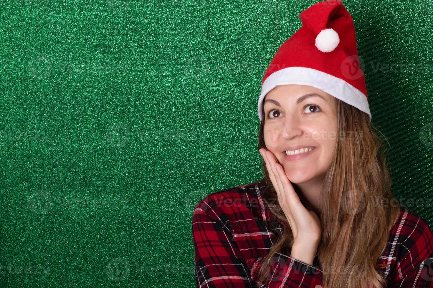 beautiful girl in a shirt on a green background in a New Year's cap smiling. Christmas. New Year. photo