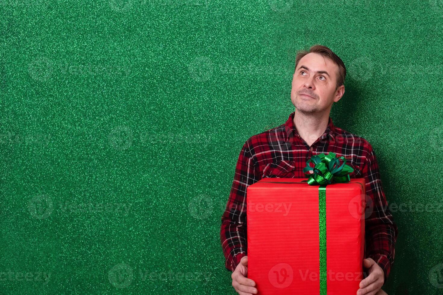 smiling man with a large gift in his hands on a green background. holiday. New Year. Valentine's Day. man looking at green background photo