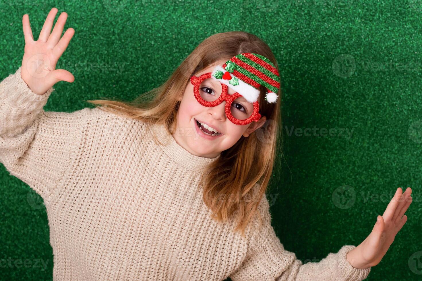 a cute girl in New Year's souvenir glasses with a New Year's cap on a green background laughs. New Year's background photo