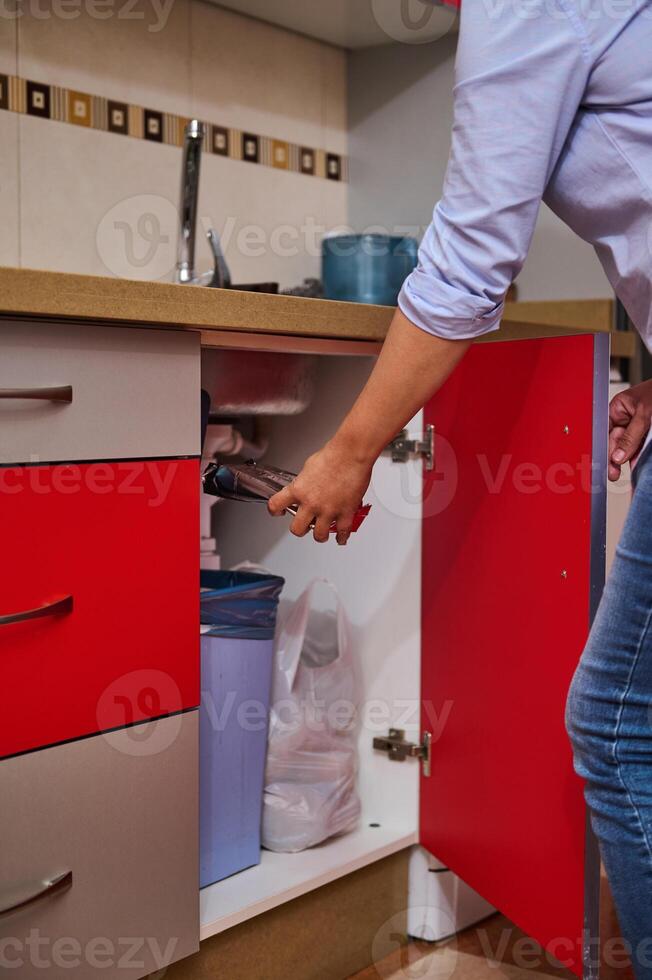Person fixing a kitchen sink with a red cabinet open photo