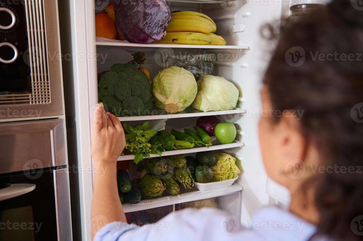 Woman looking inside refrigerator full of fresh fruits and vegetables photo