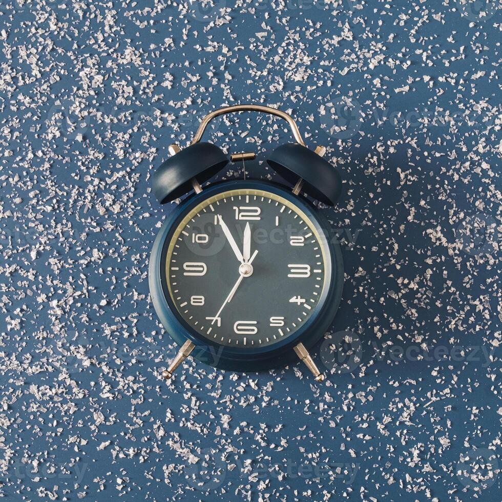 Alarm clock over a cold blue background with scattered snow photo