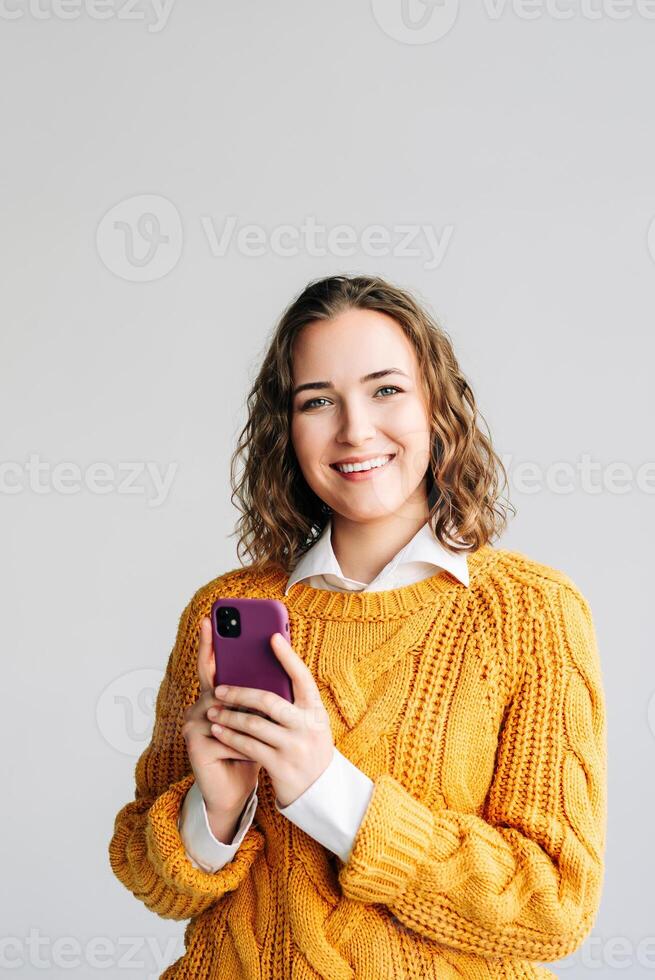 Young Business Woman Using Smartphone at White Background. A portrait of a smiling young businesswoman holding a smartphone, engaged in browsing apps, checking online content, and texting messages. photo