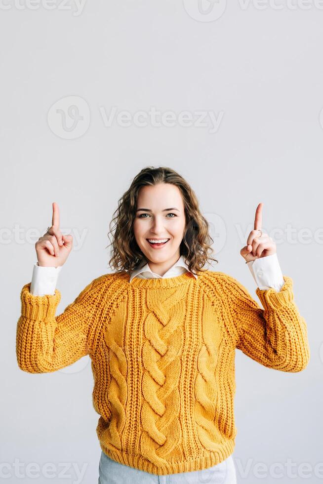Excited Woman Pointing Upward. Enthusiastic young woman with curly hair, smiling and pointing upward. Isolated against a white background, ideal for promoting products, services, sales photo