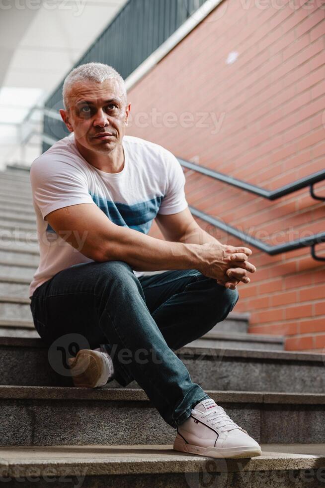 A man in a white shirt and blue jeans is sitting on a set of stairs photo
