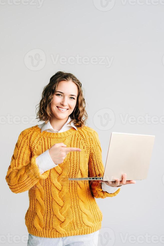 Student Presenting E-Learning on Laptop. A young woman enthusiastically points at a laptop, showcasing e-learning courses and educational software, perfect for promoting online education photo