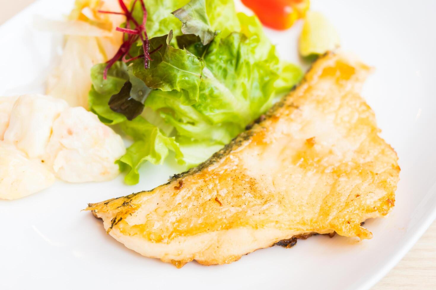 A piece of fish is on a plate with a salad photo