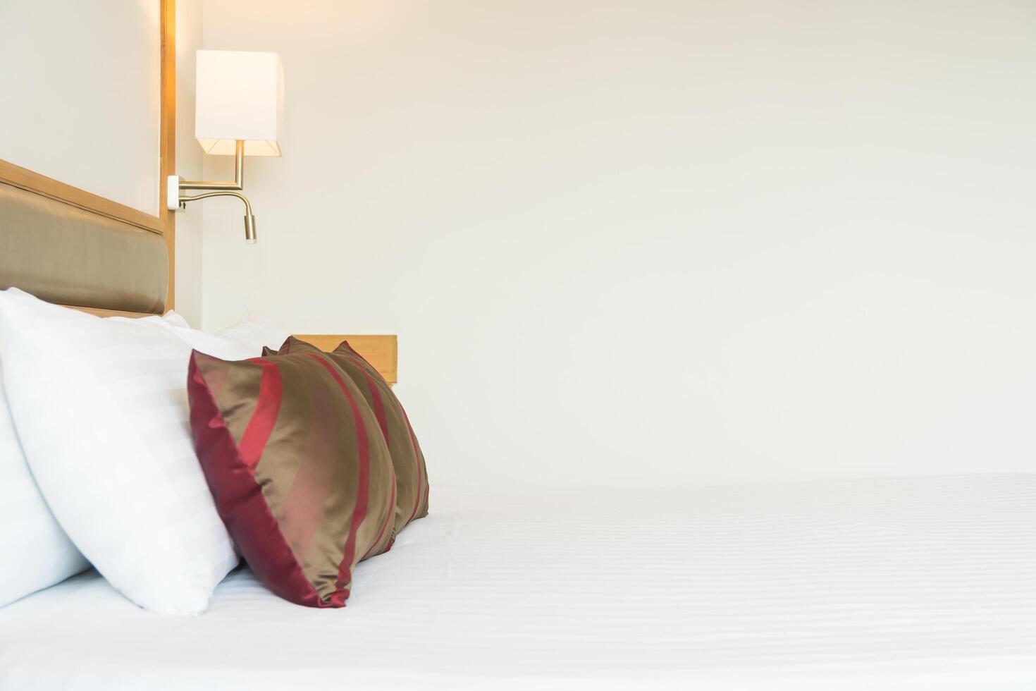 A white bed with red pillows and a lamp photo