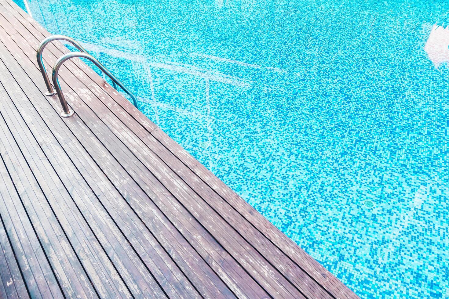 A wooden deck with a swimming pool and a ladder photo