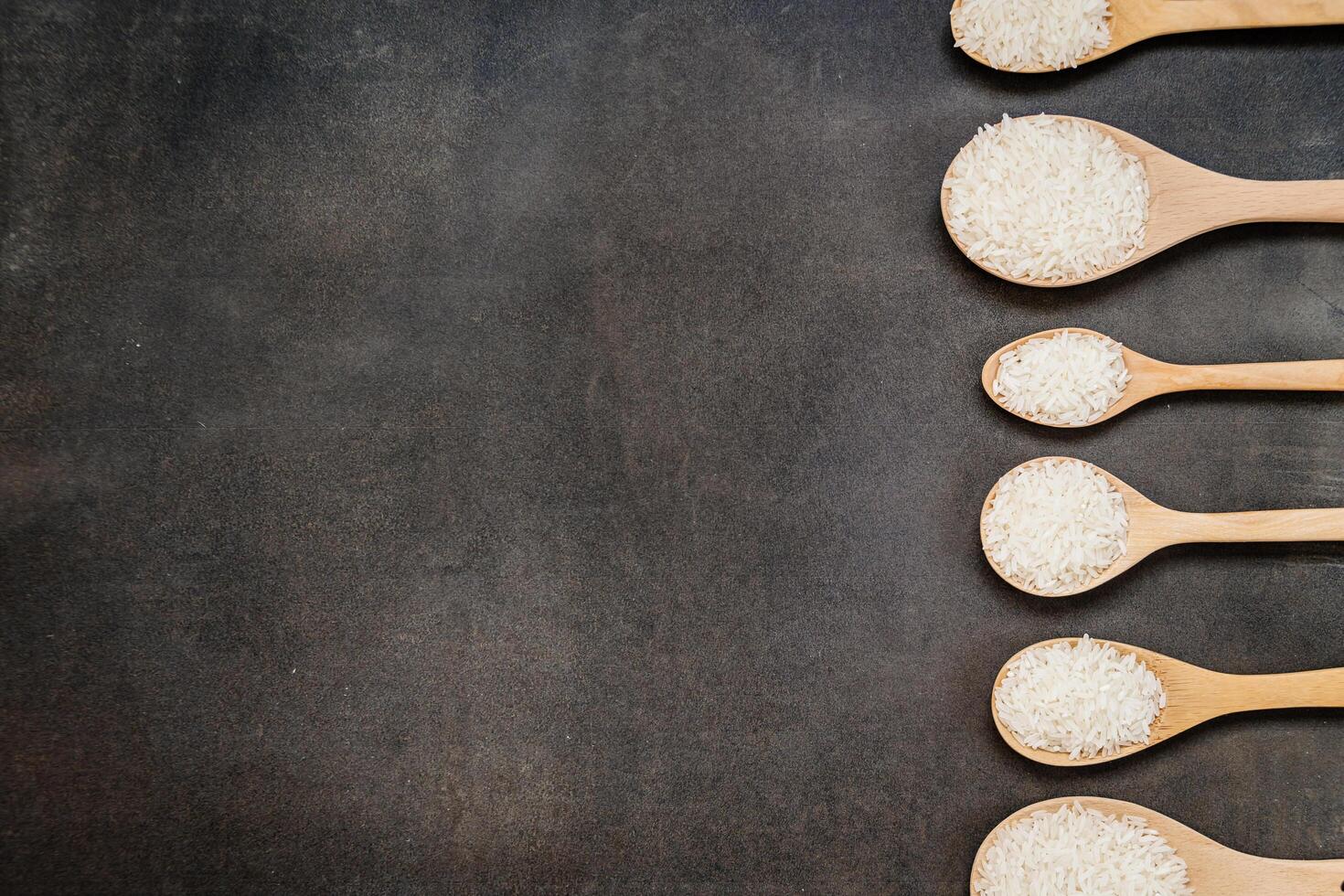 Six wooden spoons with rice in them on a black background photo