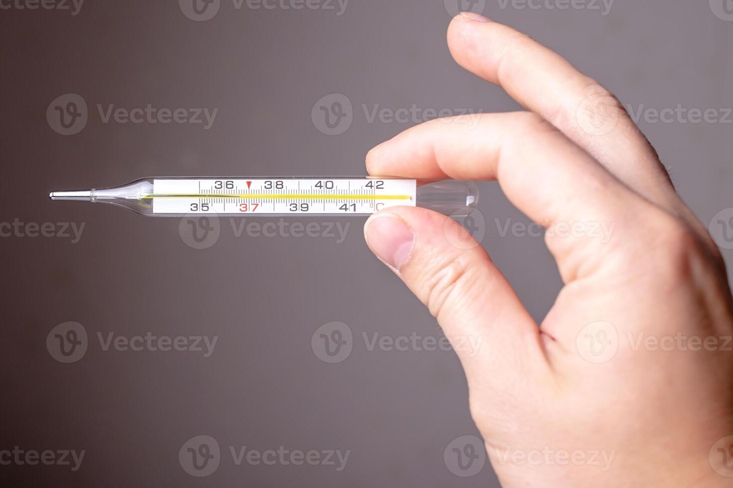 Hand holds a medical mercury thermometer with normal temperature, on a gray background. photo