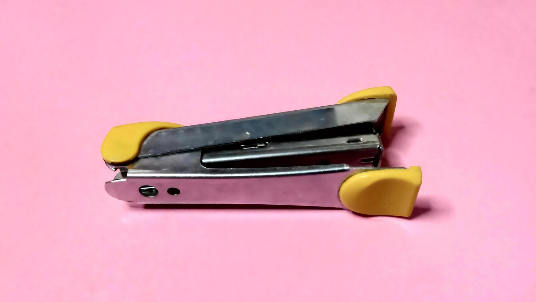 Close up of a yellow and silver stapler on a pink background. Office supplies, stationery, simple design. photo