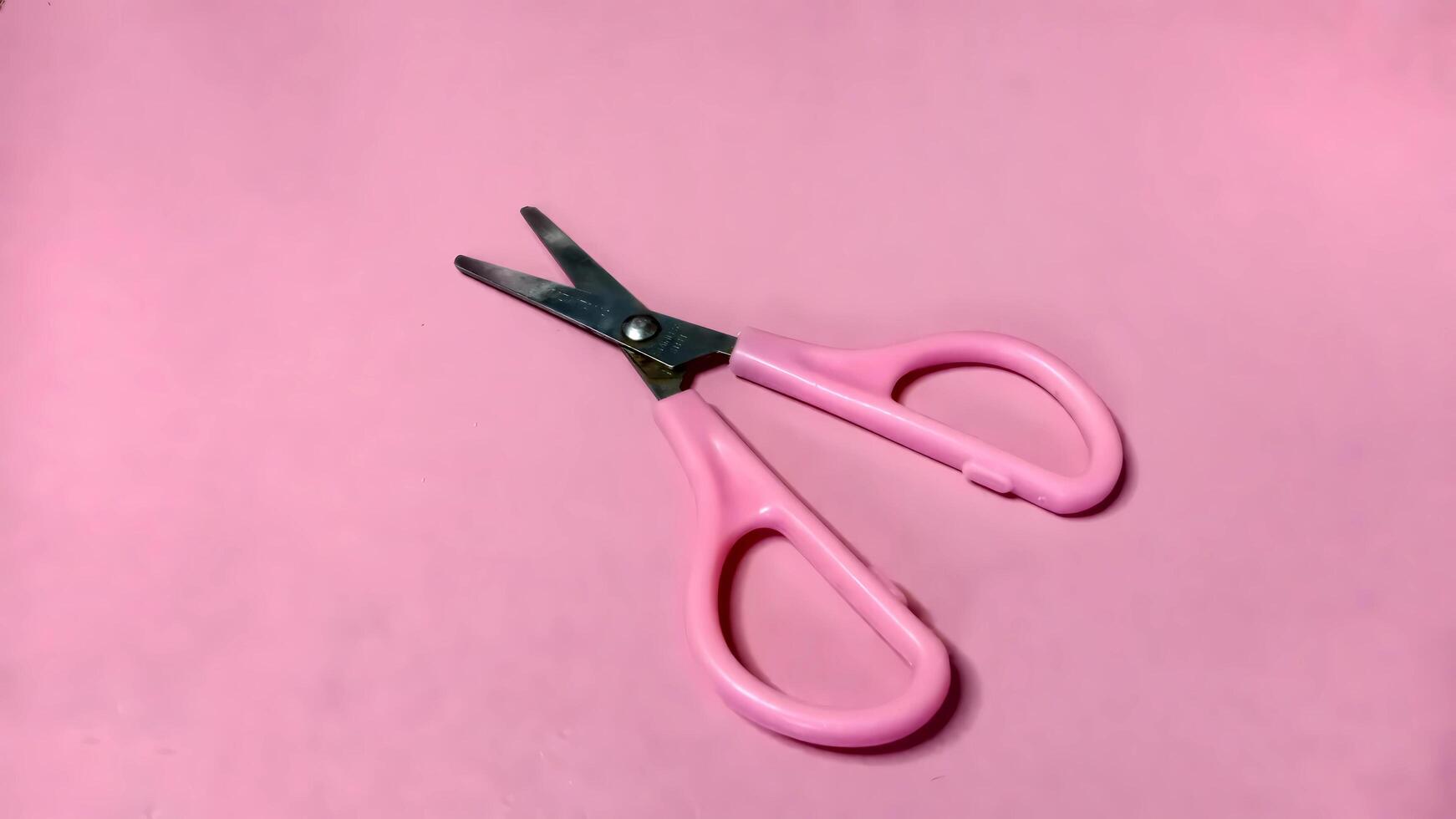 Small pink scissors on a pink background. Concept of cutting, crafting, and precision. photo