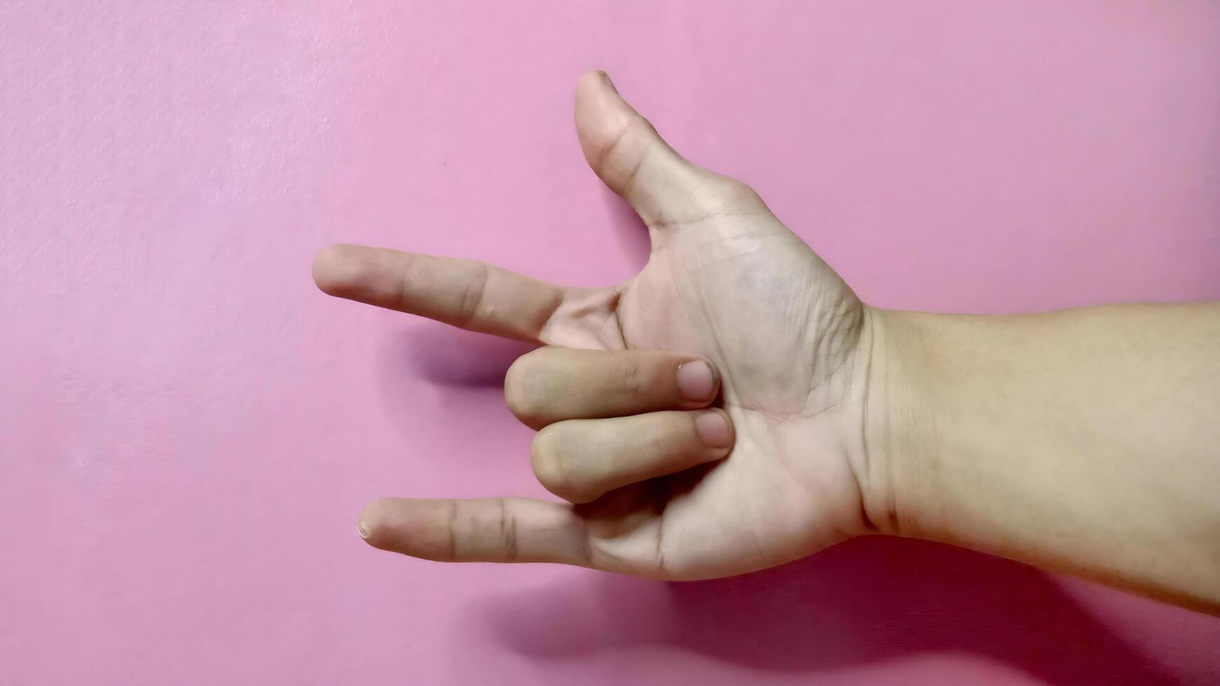 Close up of a hand forming the 'I love you' sign language against a pink background. Concept of love, affection, and communication. photo