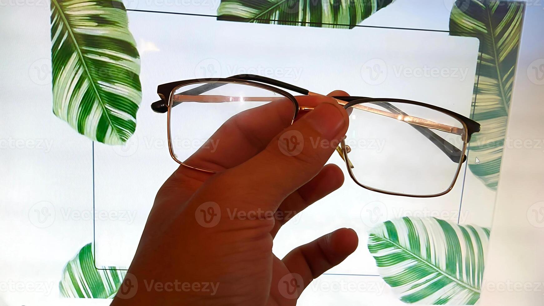 Stylish Eyeglasses Held in Hand Against Tropical Leaves. Concept of Vision, Fashion, Optics, Summer photo