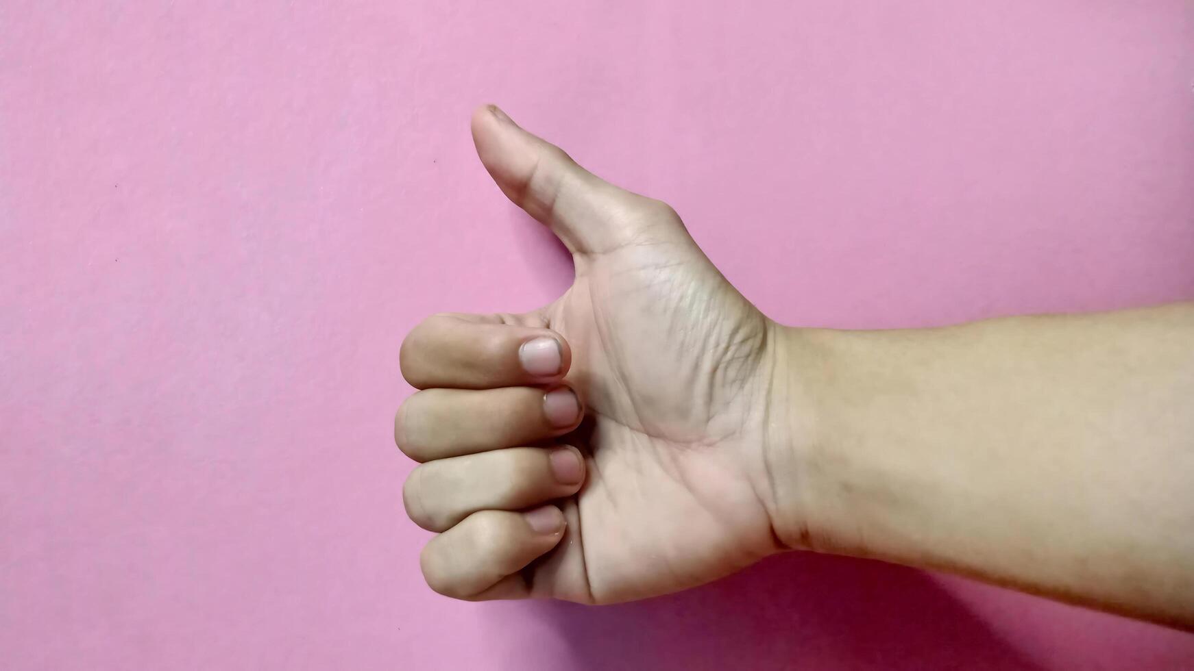 Close up of hand gesturing thumbs up against a pink backdrop. Positive, approval, success concept. photo