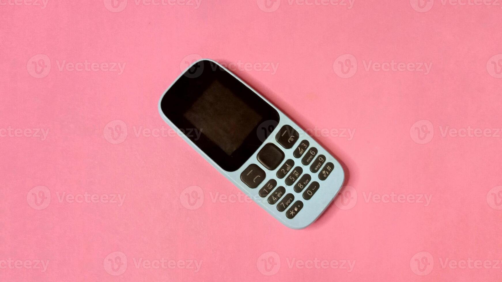 Top view of a simple mobile phone on a pink background. Minimalist concept of communication, technology, and simplicity. photo