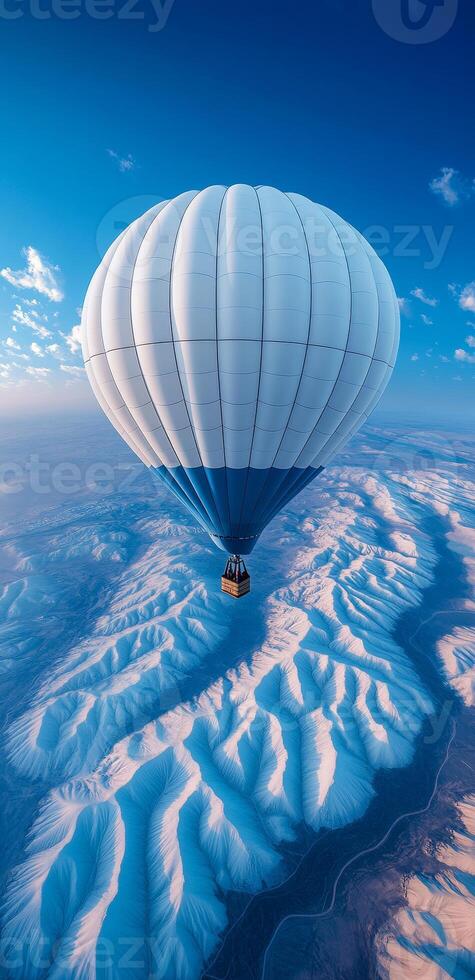 Hot air balloon soaring over snow-capped mountains. A hot air balloon floats high above stunning snow-covered mountain peaks on a clear, sunny day with blue skies. photo