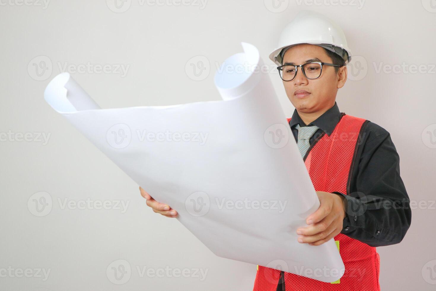 Portrait young asian man is engineer wearing helmet holding and looking blueprint with confident isolated on white background, handsome male is architect or contractor, worker or labor concept. photo