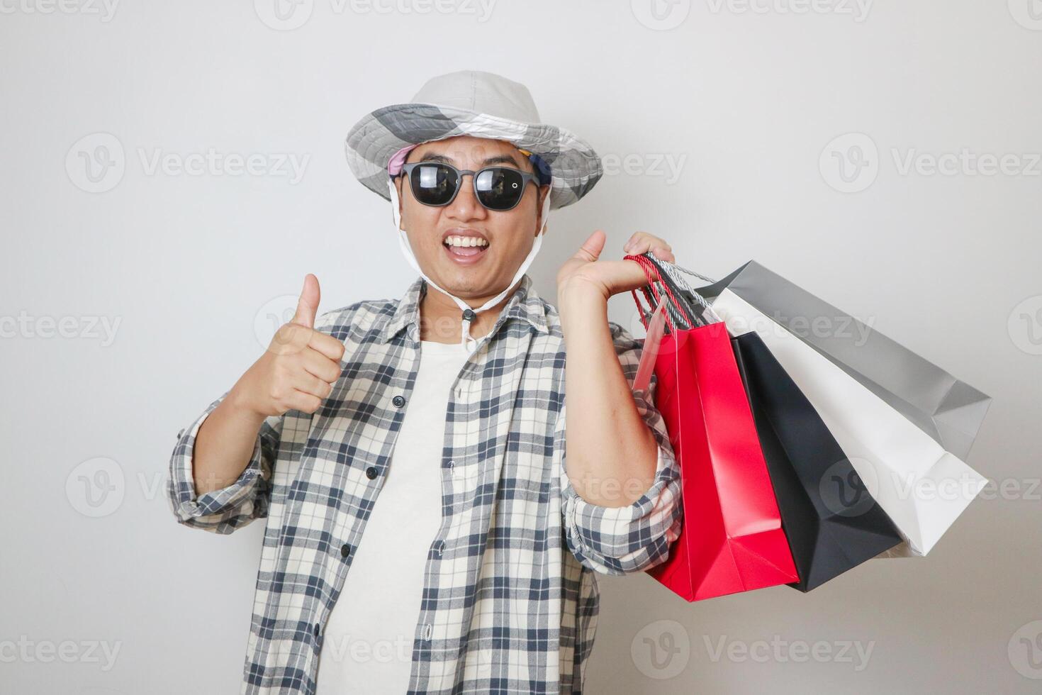 happy asian man smiling and thumb up at his hand while bring the shopping bags on isolated background photo