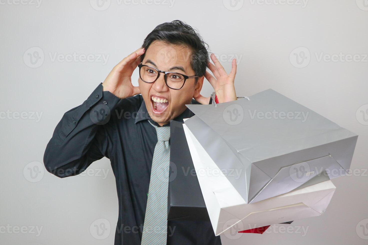 Portrait of young Asian man shouting and holding shopping bags in pose on white background. photo
