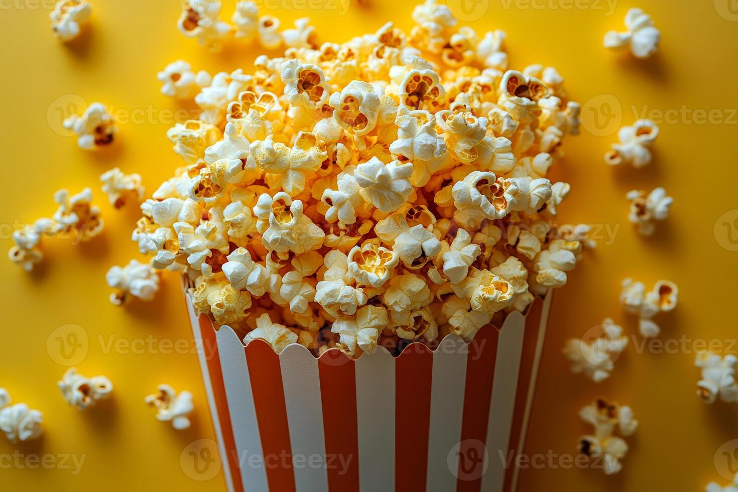 A large bowl of popcorn is sitting on a yellow background. The popcorn is in a paper bag with orange and white stripes photo