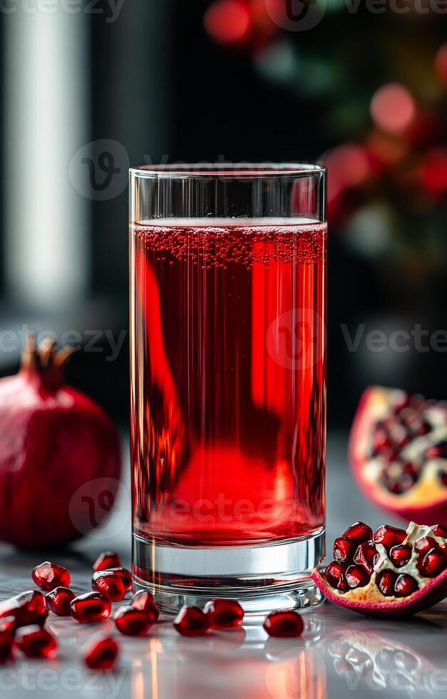 Pomegranate juice in a tall glass. A tall glass of vibrant pomegranate juice beside fresh pomegranates and seeds on a marble surface in soft light. photo