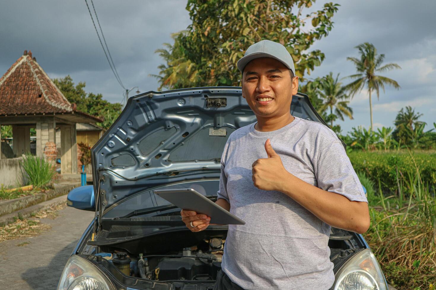 Happy asian automobile mechanic repairman wearing uniform and holding tablet, He standing and thumb up to camera After repairing the car, car service and maintenance, Repair service. photo