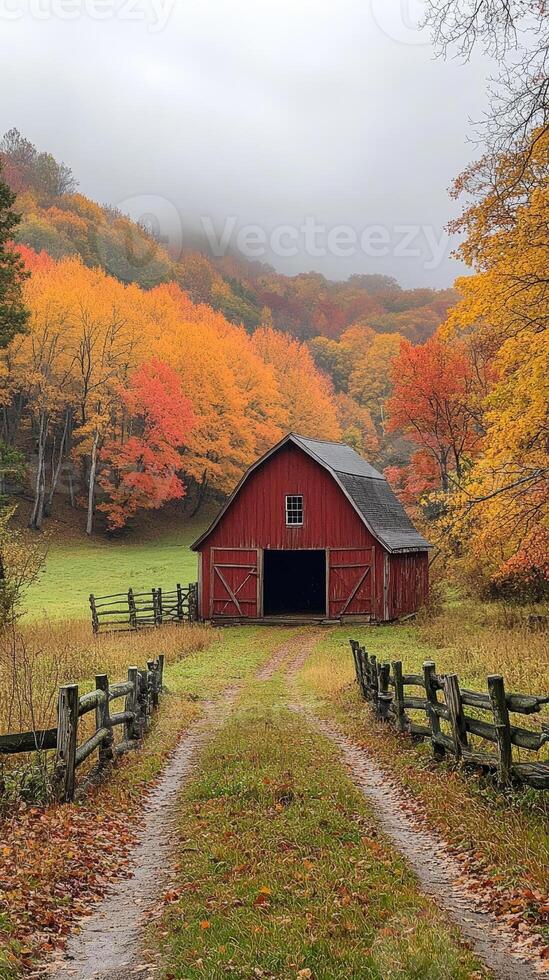 A red barn at the end of a dirt path is framed by colorful fall trees beneath a cloudy sky. photo