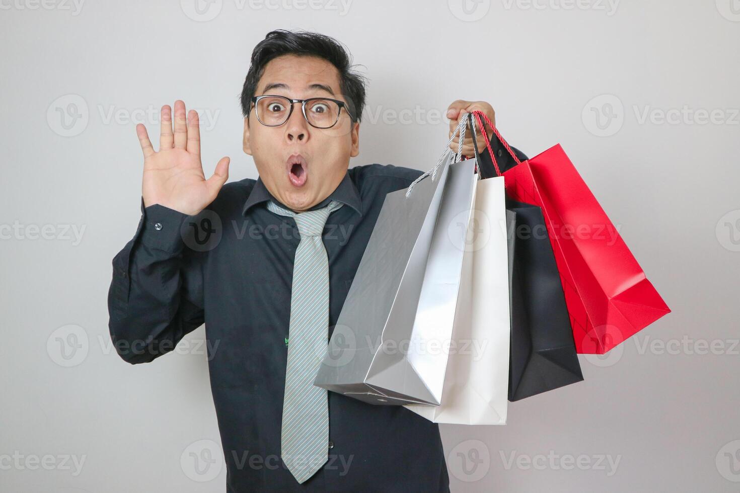 Portrait of young Asian man with surprised expression while holding shopping bags and posing on white background photo