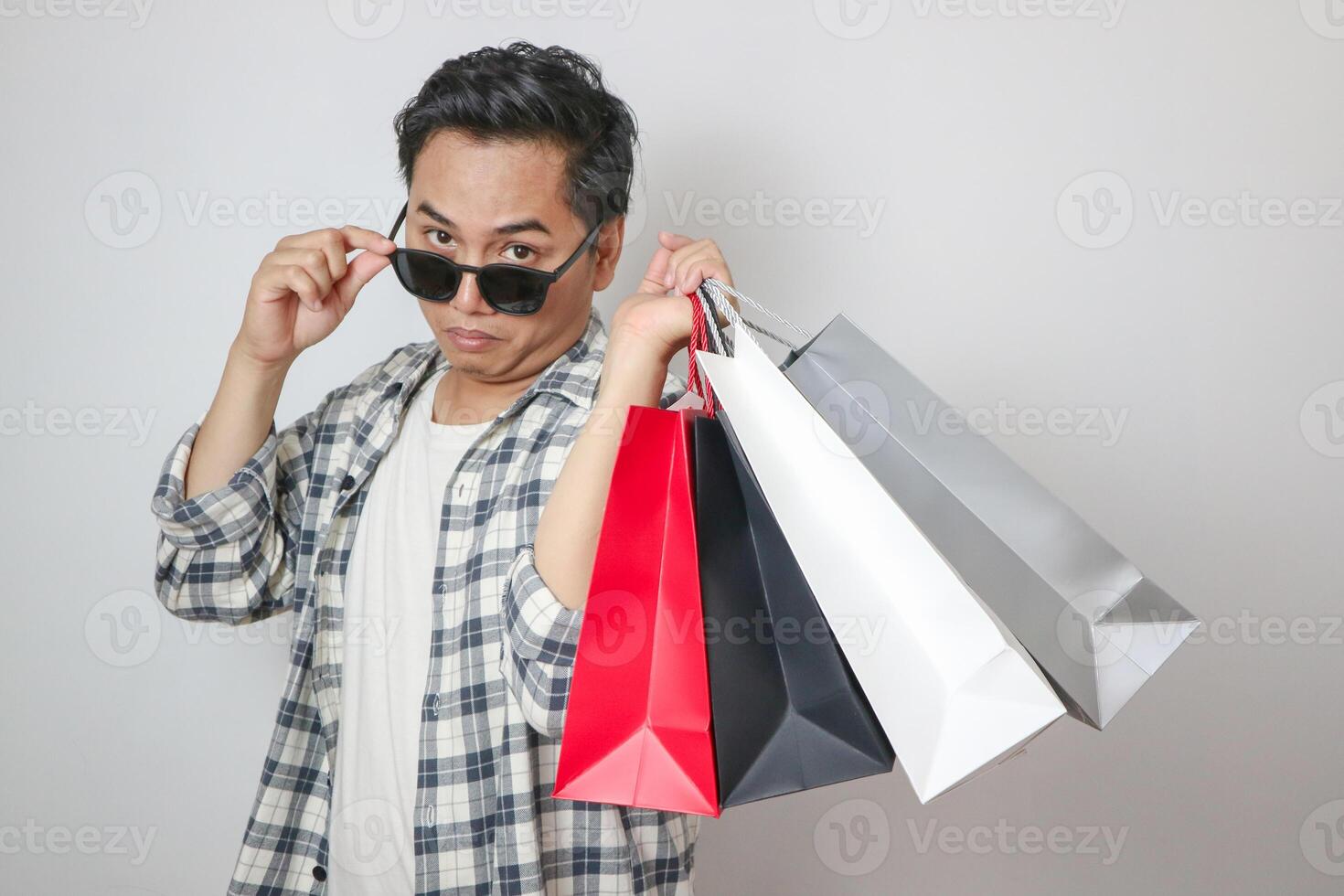 Young asian man surprised and surprised, lowering glasses looking while holding shopping bags while looking at camera with open mouth isolated on plain white background studio portrait. photo