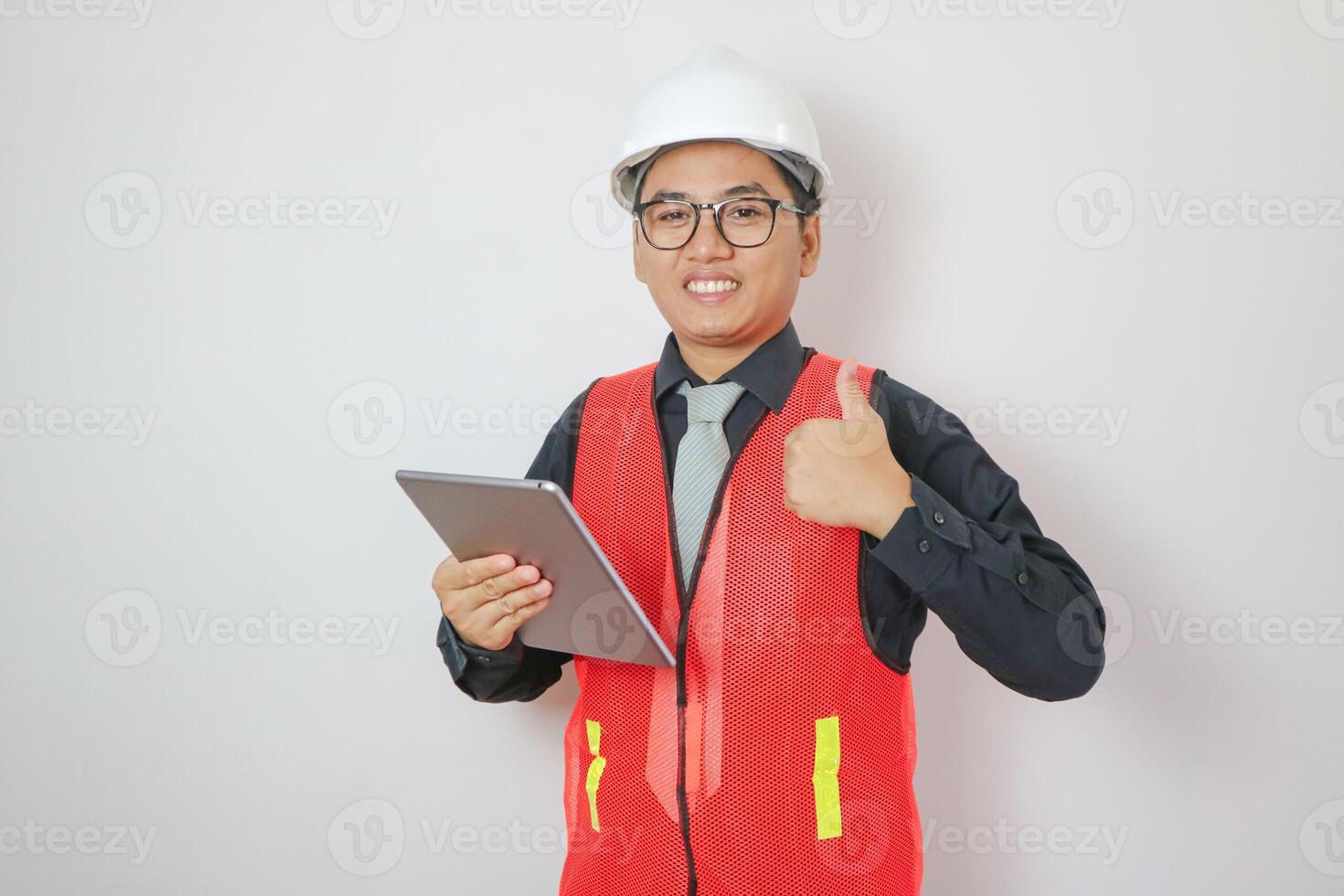 Portrait of happy young handsome Indian male civil engineer or architect wearing helmet at construction site. photo