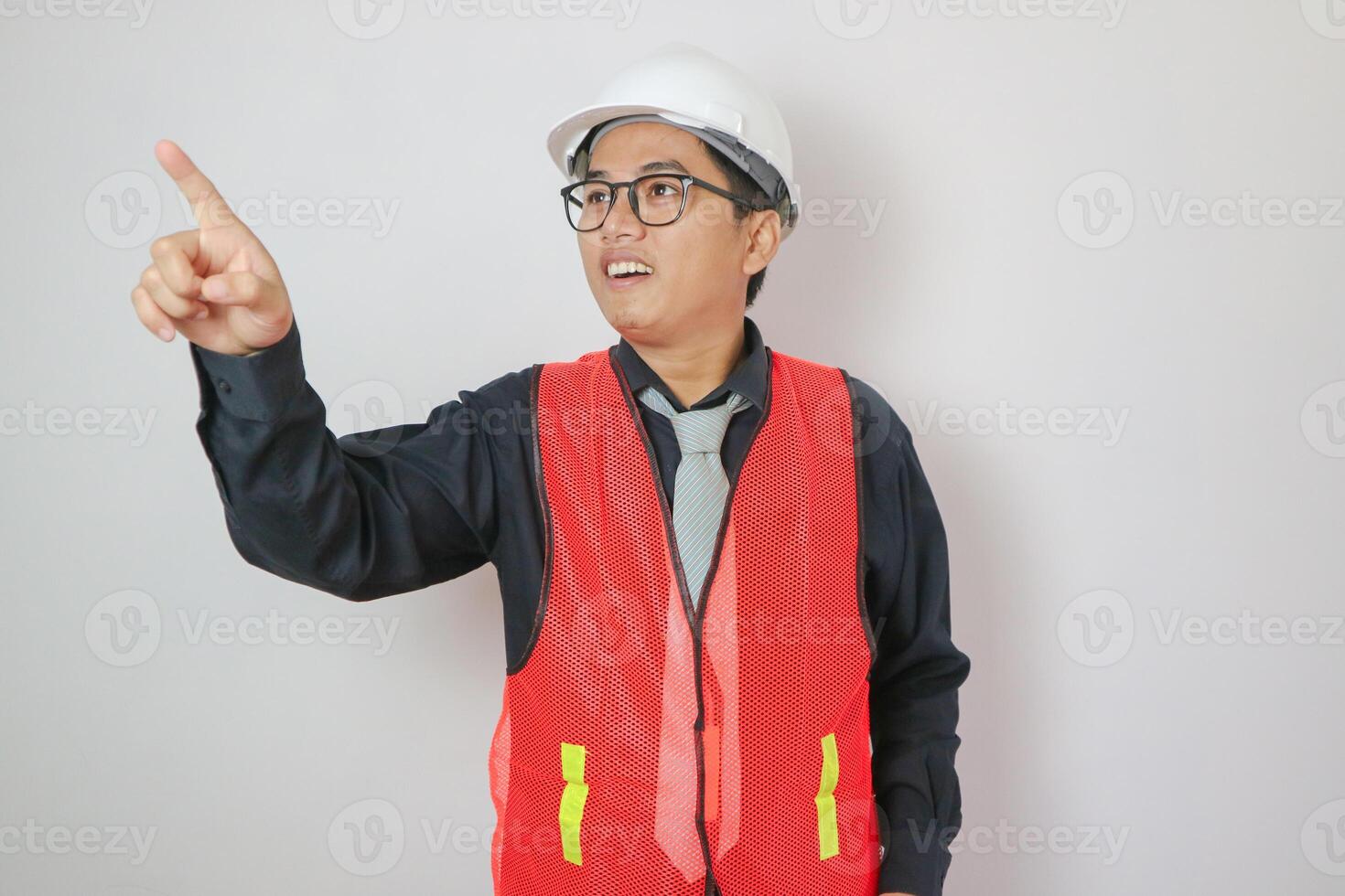 architecture, construction business and people concept - smiling asian male architect in helmet pointing finger to something over grey background photo