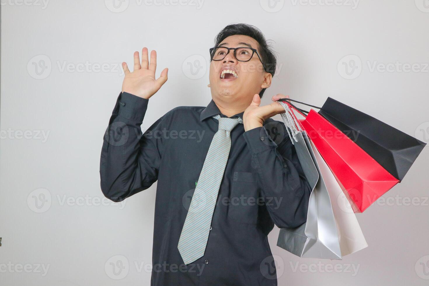 Portrait of young Asian man with surprised expression while holding shopping bags and posing on white background photo