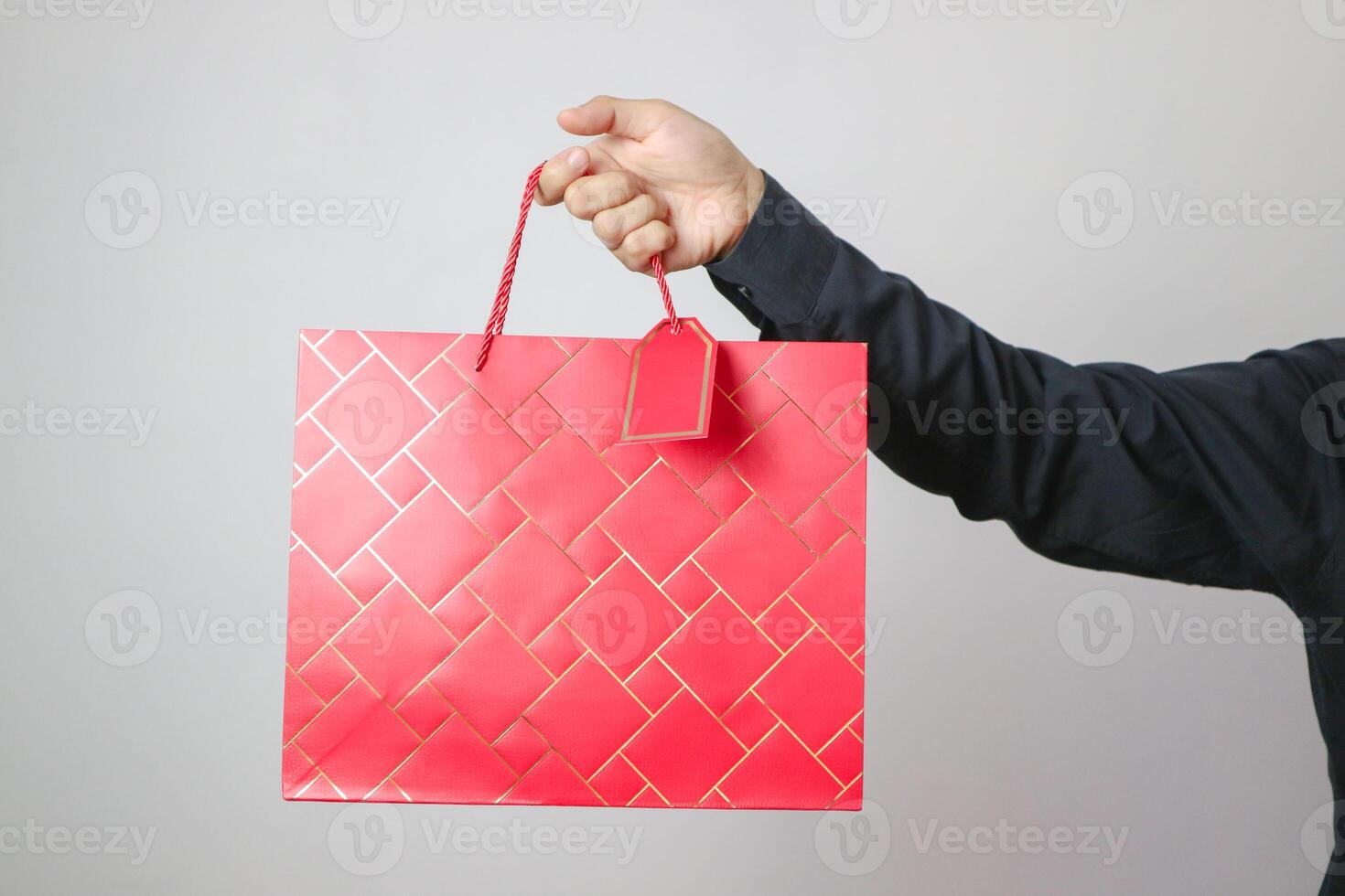 Studio image of male hand holding a bunch of red paper shopping bags isolated over bright colored white background. photo
