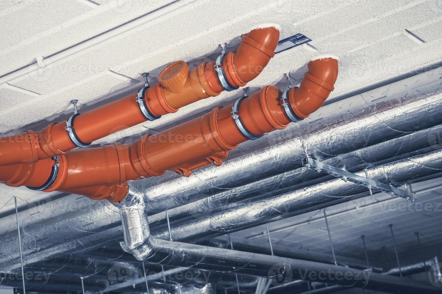 Orange Plastic Pipes and Metallic Ducts Installed on a Ceiling in a Commercial Building photo