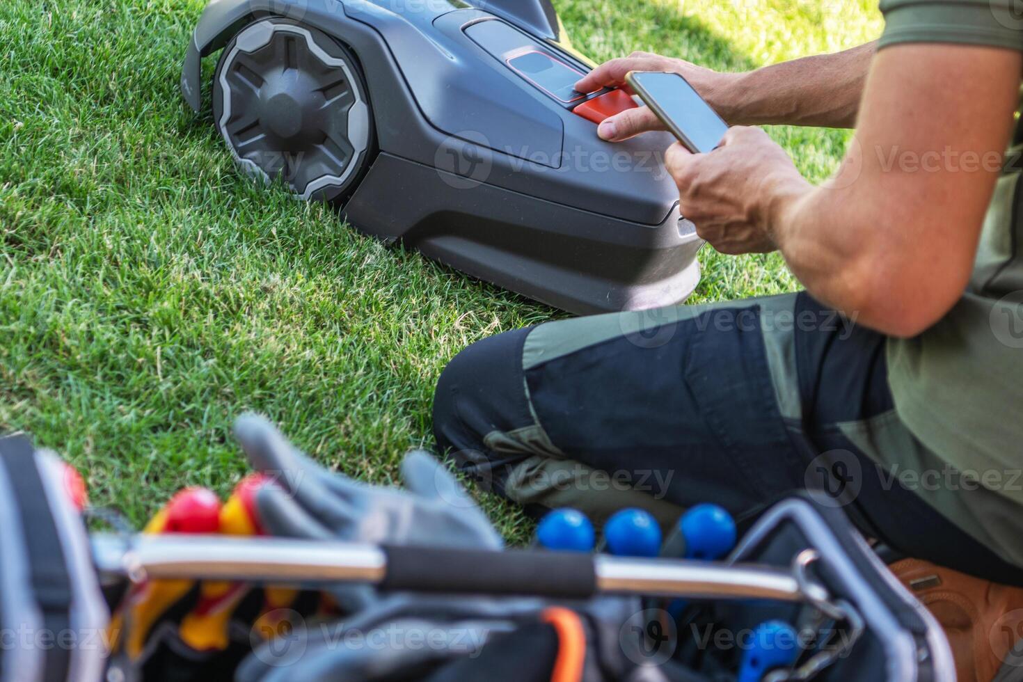 Person Operating a Robotic Lawn Mower While Preparing Tools for Landscaping Work photo