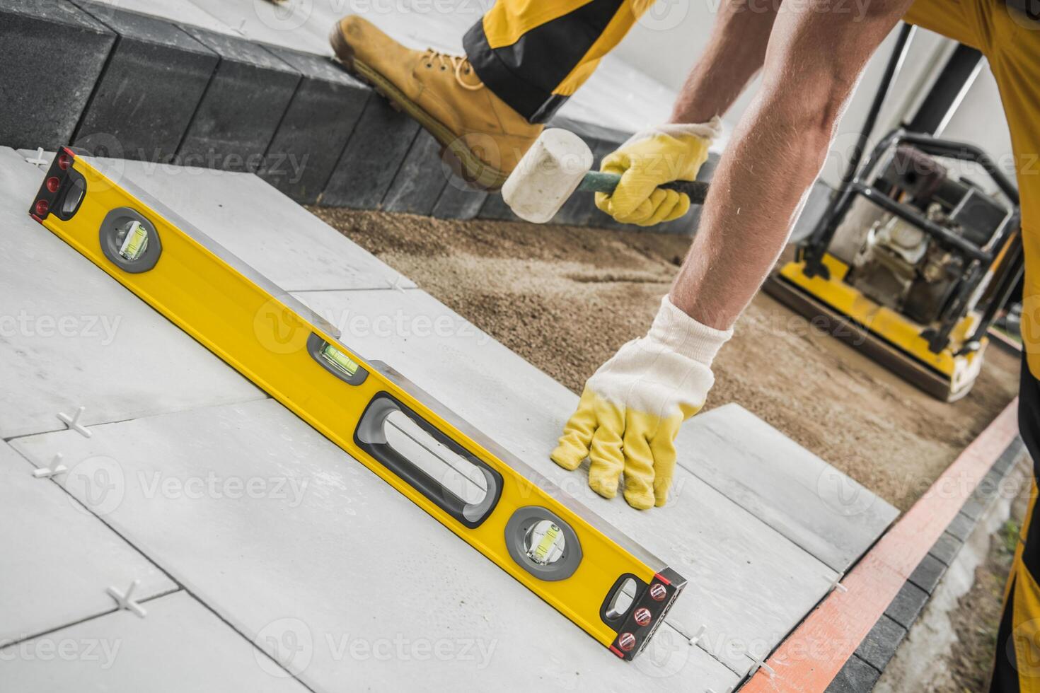 Worker Using a Level Tool to Ensure Evenness While Laying Pavers on a Construction Site photo