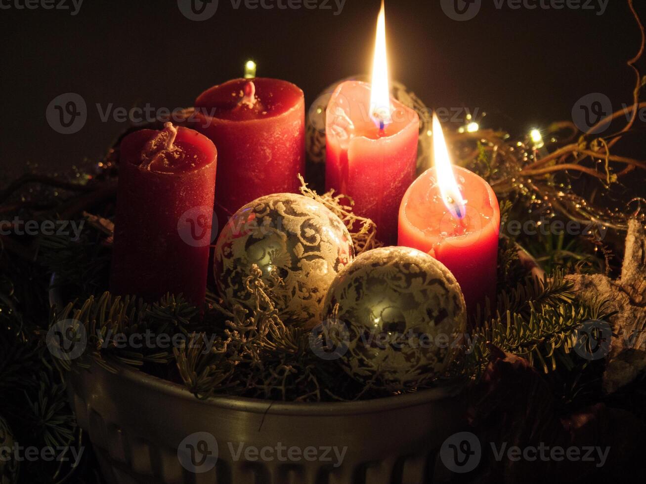 Three red candles are lit in a silver bowl with pine cones and other decorations photo