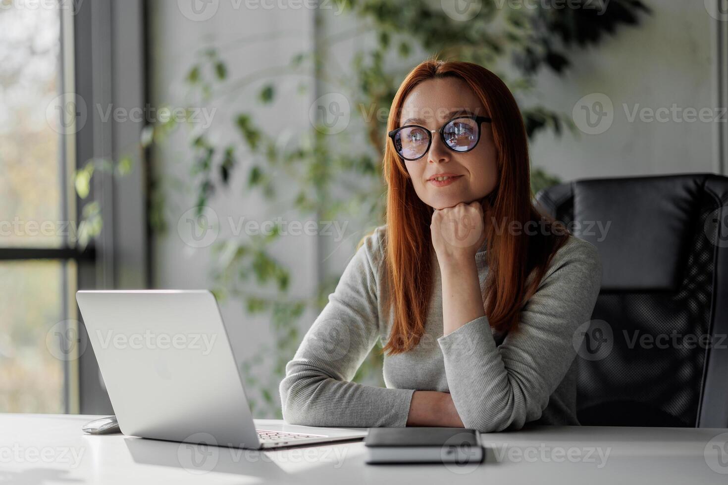 Senior chic woman using laptop at home while taking notes in notebook. Old freelancer works in the living room on a laptop while drafting details on a book. photo