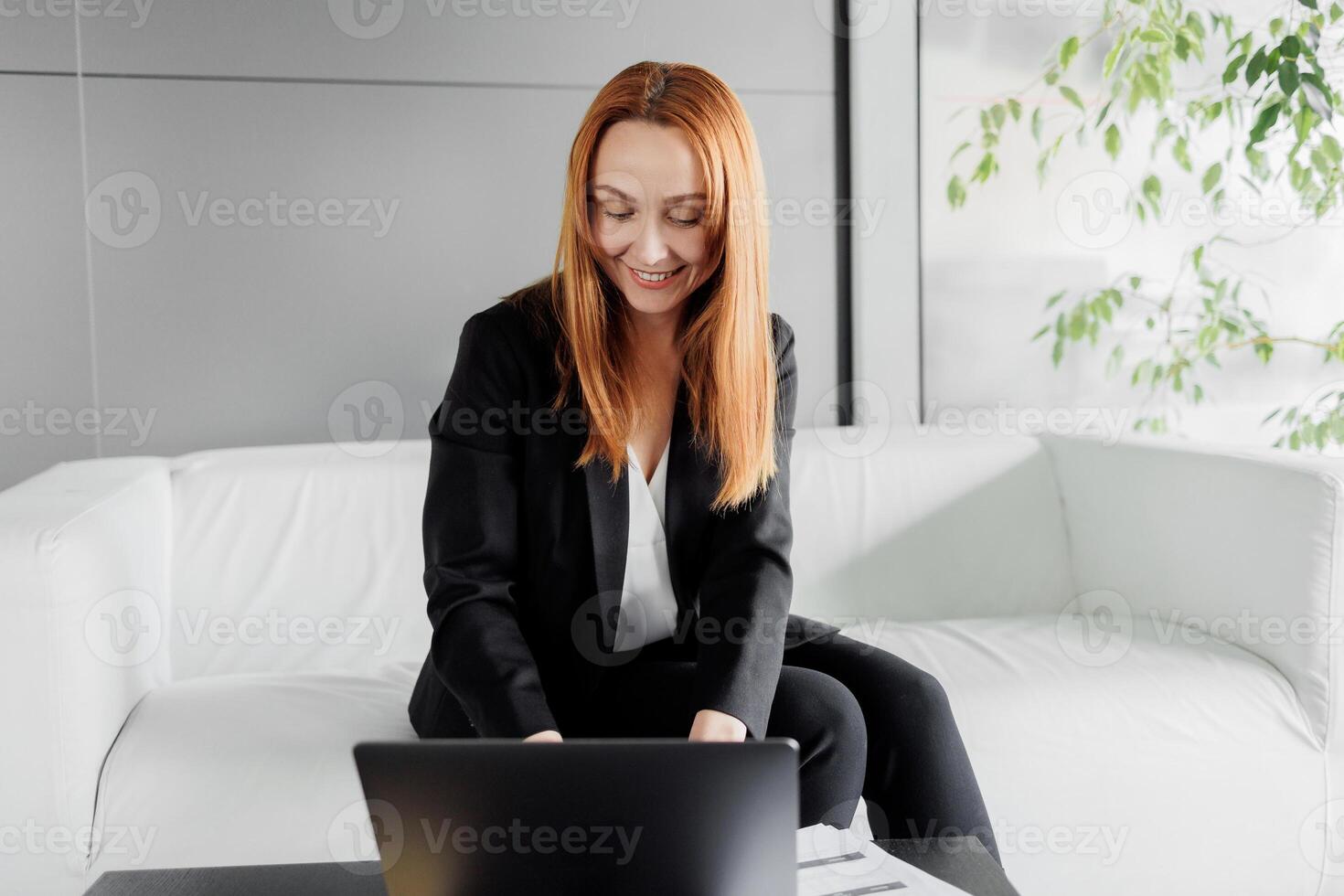 Mid aged business woman in an office with a laptop in front of her. Web conference, online working, remotely managing the business. photo