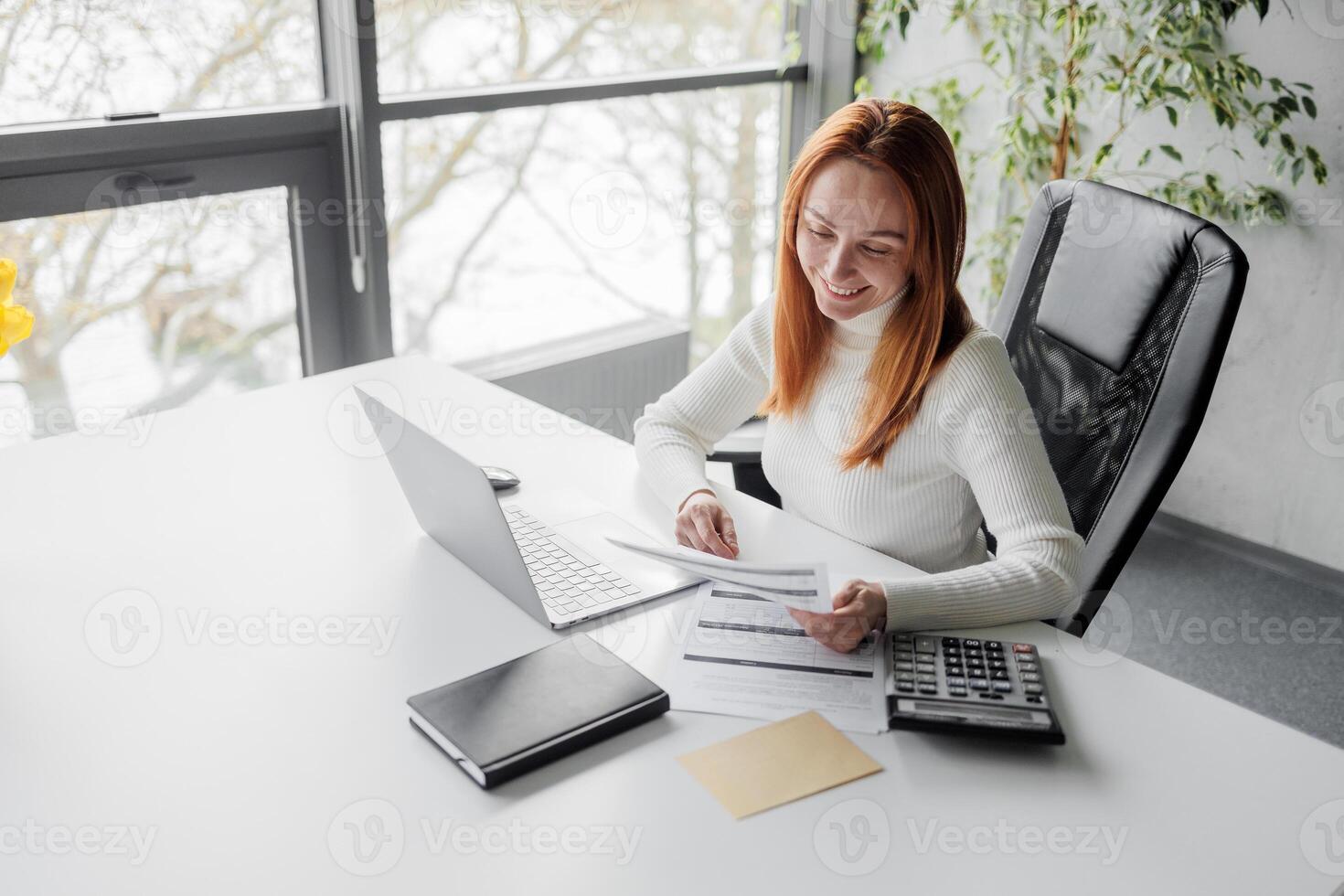 Happy, sophisticated, and elderly woman taking notes while working remotely from home. smiling middle-aged business woman watching webinar on computer. photo