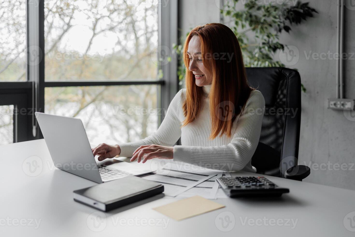 Happy, sophisticated, and elderly woman taking notes while working remotely from home. smiling middle-aged business woman watching webinar on computer. photo
