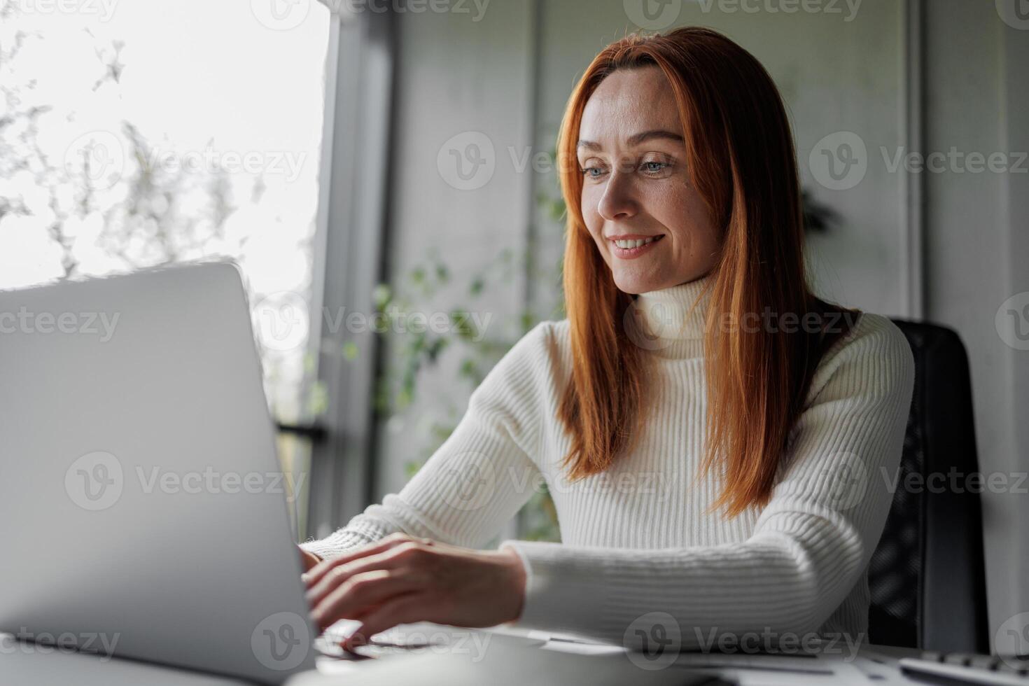 Happy, sophisticated, and elderly woman taking notes while working remotely from home. smiling middle-aged business woman watching webinar on computer. photo