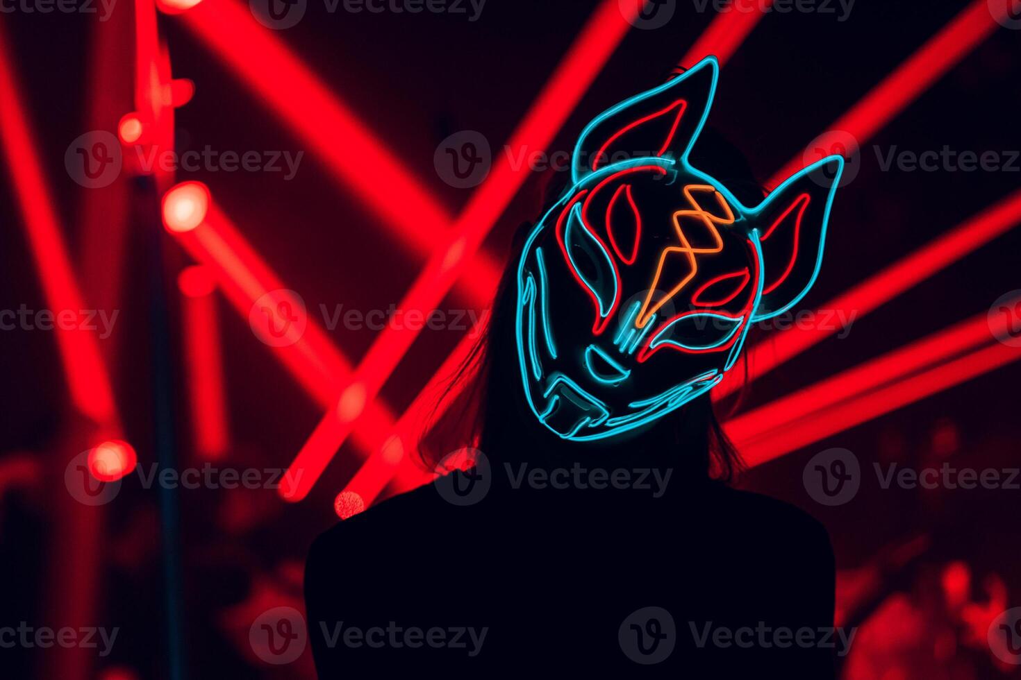 Illuminated Mystery A vibrant figure shrouded in a glowing mask stands against a backdrop of pulsating red light beams, merging intrigue with electrifying energy. photo