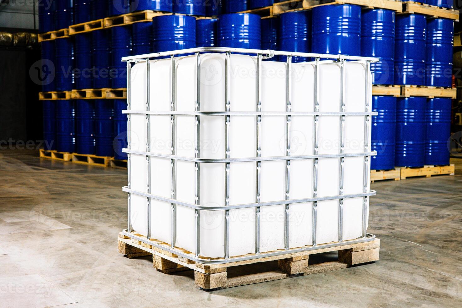 Industrial Harmony A Sturdy Liquid Storage Container Nestled on a Pallet, Surrounded by a Sea of Vibrant Blue Barrels photo