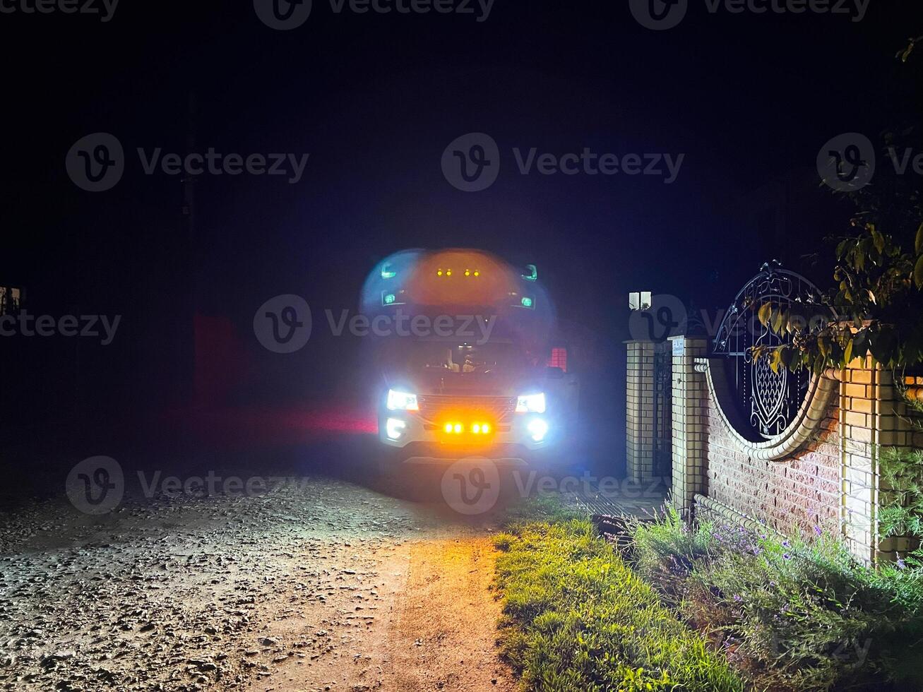 Truck with bright headlights parked near a gated entrance at night photo