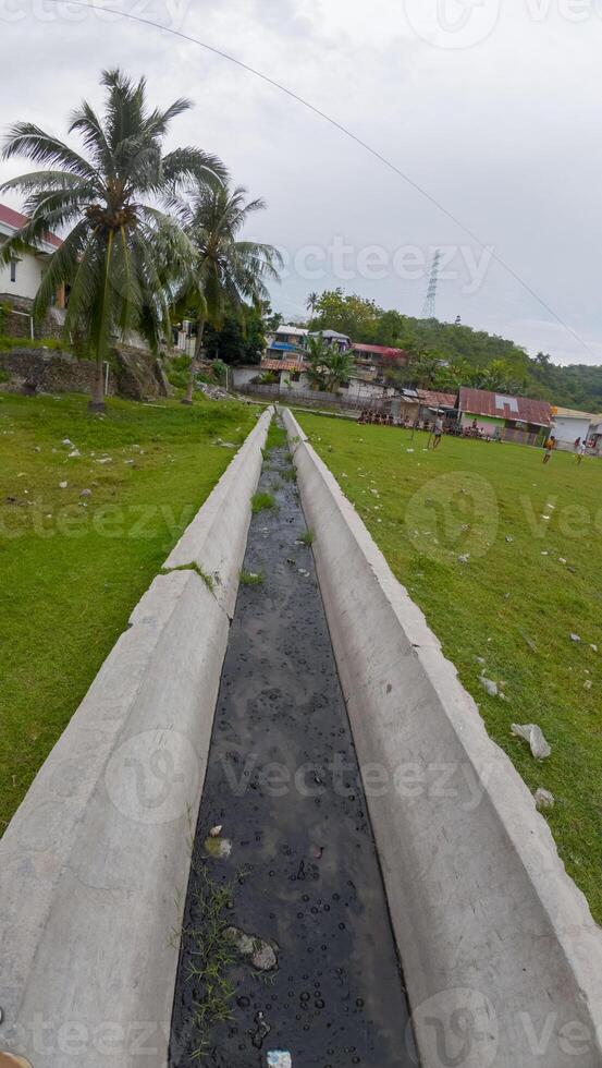 Concrete drainage pipe with dirty water and green grass in the garden photo