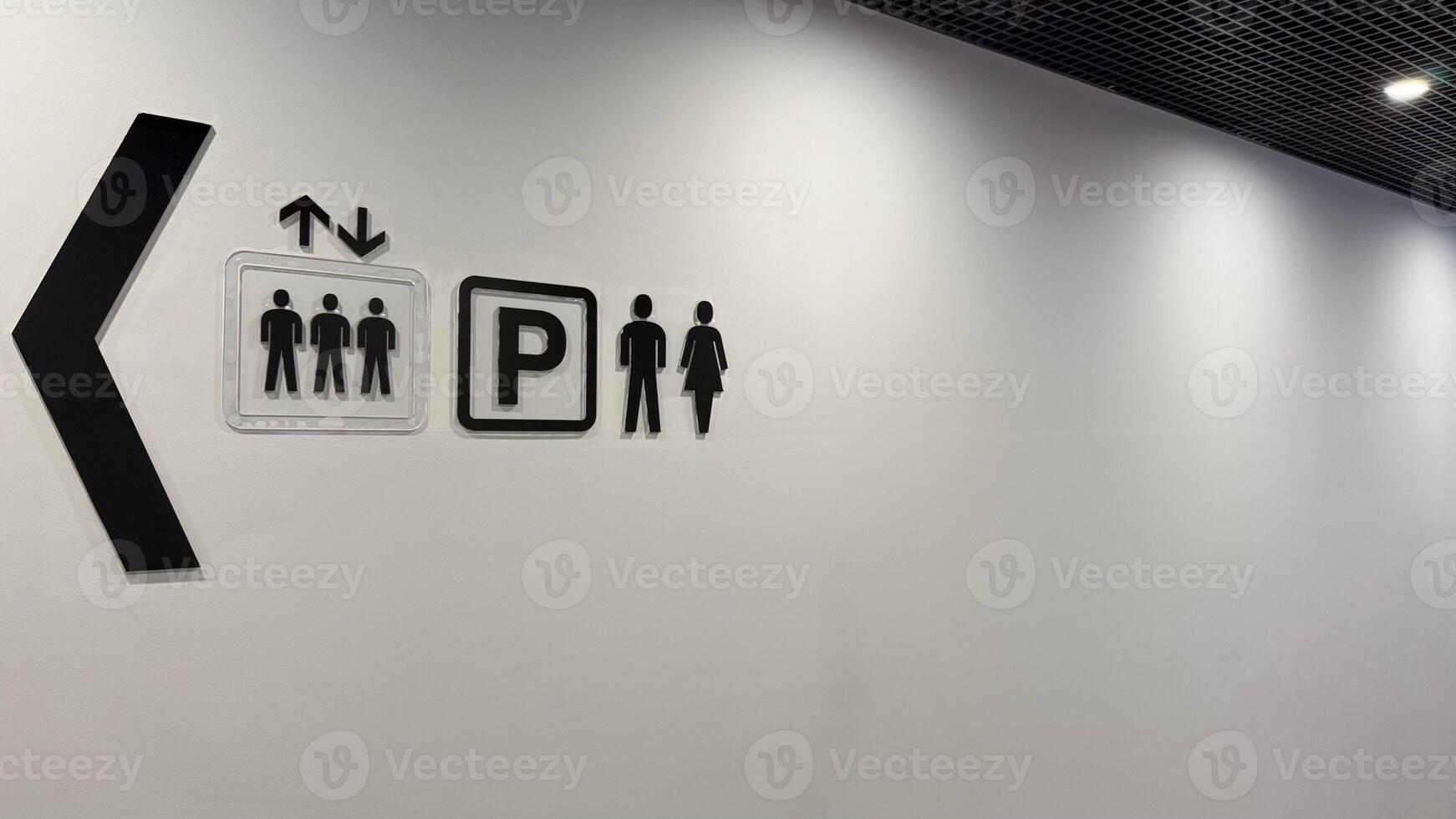 Signs on wall of shopping center with direction of movement to help with orientation, signs in corridor towards elevator, parking and toilet in public building photo
