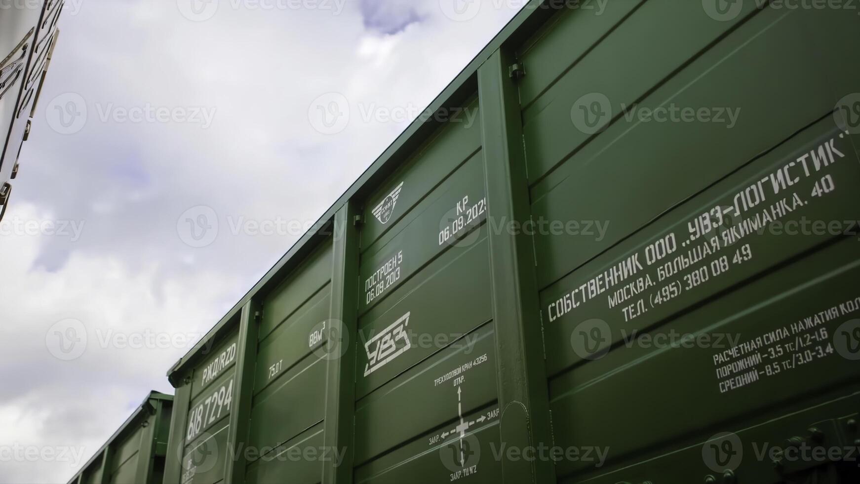 A green train car with English and Russian writing under a cloudy sky photo